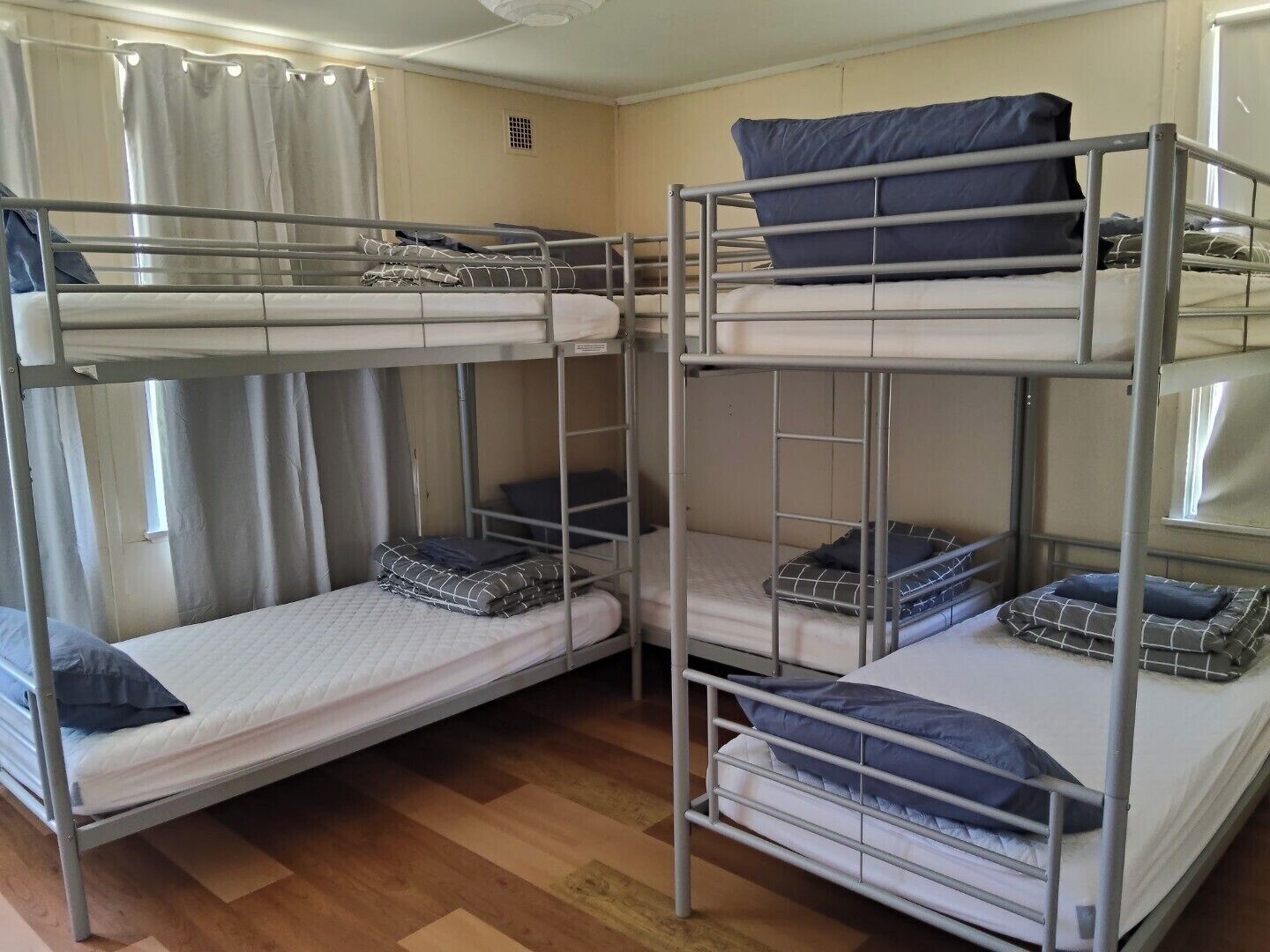 A bunk bed room with two beds, a window with curtains, and a wooden floor.