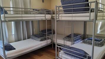 A bunk bed room with two beds, a window with curtains, and a wooden floor.