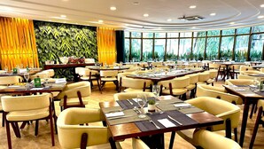 A spacious dining area with multiple tables and chairs, a large window with a view of greenery, and a wall with a leafy pattern. - Executive apartment on Paulista Avenue – across from Rosewood and Soho House SP (São Paulo)