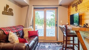 A cozy room with a leather sofa, a wooden desk with a TV, and a large sliding glass door leading to an outdoor area. - Lower Cozy Cabin in Powderhorn Ski Resort (Mesa)