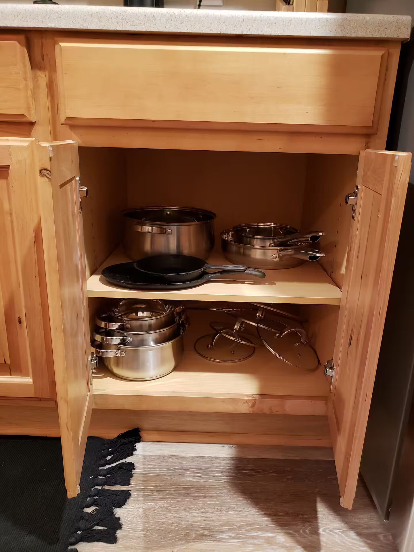 A wooden kitchen cabinet with multiple shelves holding pots, pans, and a frying pan.