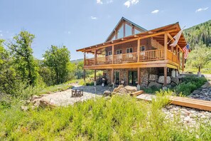 A wooden cabin with a balcony, stone foundation, and a fire pit in the yard.