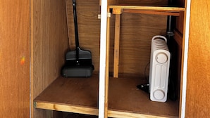 Un espacio de almacenamiento pequeño con estantes de madera, un aspirador y un radiador.