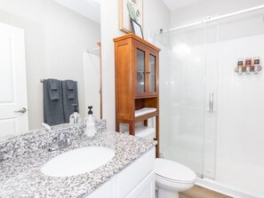 Une salle de bain avec un lavabo sur un comptoir en granit, un meuble en bois avec des portes en verre, des toilettes et une douche fermée par des parois en verre.