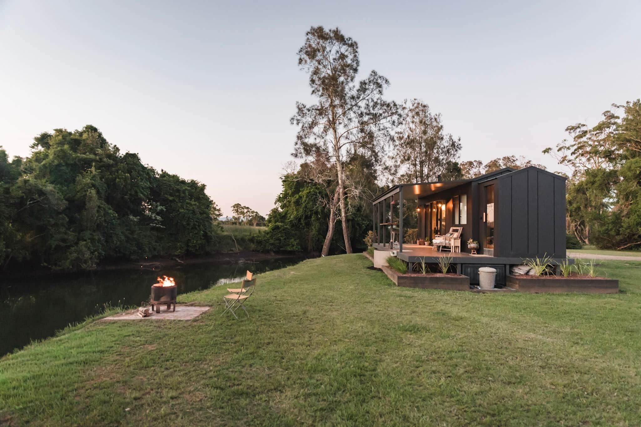 Una casa moderna con un balcón que da a un lago, rodeada de árboles.