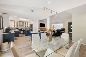 A modern kitchen with white cabinets, a central island, and a dining area with a glass table and white chairs. - 3BR Relaxing Desert Oasis  Hot Tub Pool BBQ Games (Bermuda Dunes)