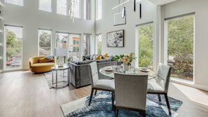A spacious living room with high ceilings, large windows, and modern furniture. - Luxury Newly Built 4 BR 4 Bath Home w/ Rooftop and Grill! (Dallas)