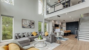 A spacious living area with a gray sofa, a round coffee table, and a yellow armchair. A staircase leads to an upper level. - Luxury Newly Built 4 BR 4 Bath Home w/ Rooftop and Grill! (Dallas)