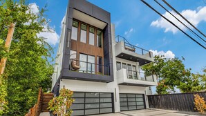 A modern two-story house with large windows, a balcony, and a garage. - Luxury Newly Built 4 BR 4 Bath Home w/ Rooftop and Grill! (Dallas)