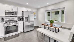 Une cuisine moderne dotée d’appareils électroménagers en acier inoxydable, un coin repas avec un banc et une grande fenêtre.