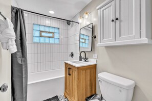 A modern bathroom with a bathtub, a wooden vanity, a toilet, and a shower curtain. - Bright & Cozy Elmhurst Stay • 3BR/2BA (Elmhurst)