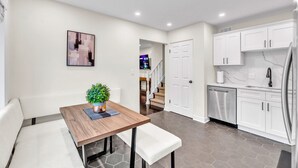 Une cuisine moderne avec des meubles blancs, un réfrigérateur en acier inoxydable et un coin repas comprenant une table et un banc en bois.