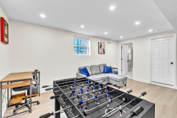 A modern living room with a foosball table, a sofa, and a desk. - Bright & Cozy Elmhurst Stay • 3BR/2BA (Elmhurst)