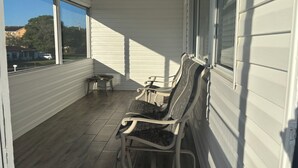 Overdekt terras met drie stoelen en een kleine tafel, grote ramen en uitzicht op een woonwijk.