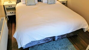 A neatly made bed with a white duvet, two bedside tables with lamps, and a small drawer unit.
