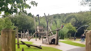 A playground with wooden structures, a winding path, and a picnic area.