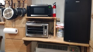 Una cocina con microondas, tostadora y un refrigerador negro. Hay ollas colgando y un extintor en la pared.