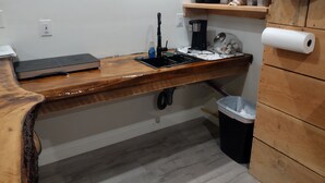 Una cocina con encimera de madera, cafetera, lavamanos y cubo de basura.