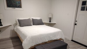 Un dormitorio con cama, mesita de noche, lámpara y puerta.