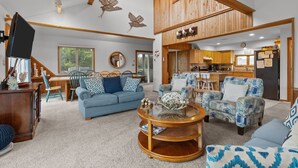 A spacious living area with a high ceiling, wooden beams, and a kitchen area with wooden cabinets and a black refrigerator. - 3946 - Summers by the Sea - Duck OBX Retreat w/ Pool & Hot Tub Near Beach (Duck)