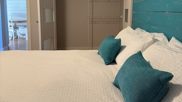 Une chambre à coucher avec un lit, des coussins de couleur turquoise, une tête de lit blanche et un dressing avec des étagères.