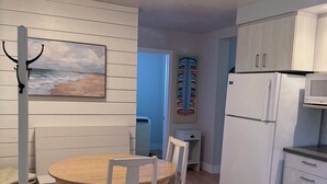 Une cuisine moderne avec des armoires blanches, un four encastré et un four à micro-ondes. On y trouve également un coin repas avec une table en bois et des chaises blanches.