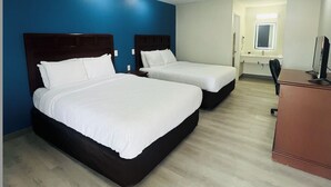 A hotel room with two beds, a desk, and a window.
