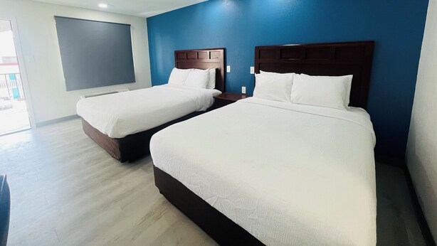 A hotel room with two beds, a large window, and a blue accent wall.