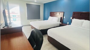 A hotel room with two beds, a wooden desk, and a chair.