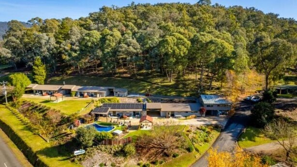 A residential area with multiple houses, a swimming pool, and a forested hill in the background. - Snowview Holiday Units (Tawonga South)