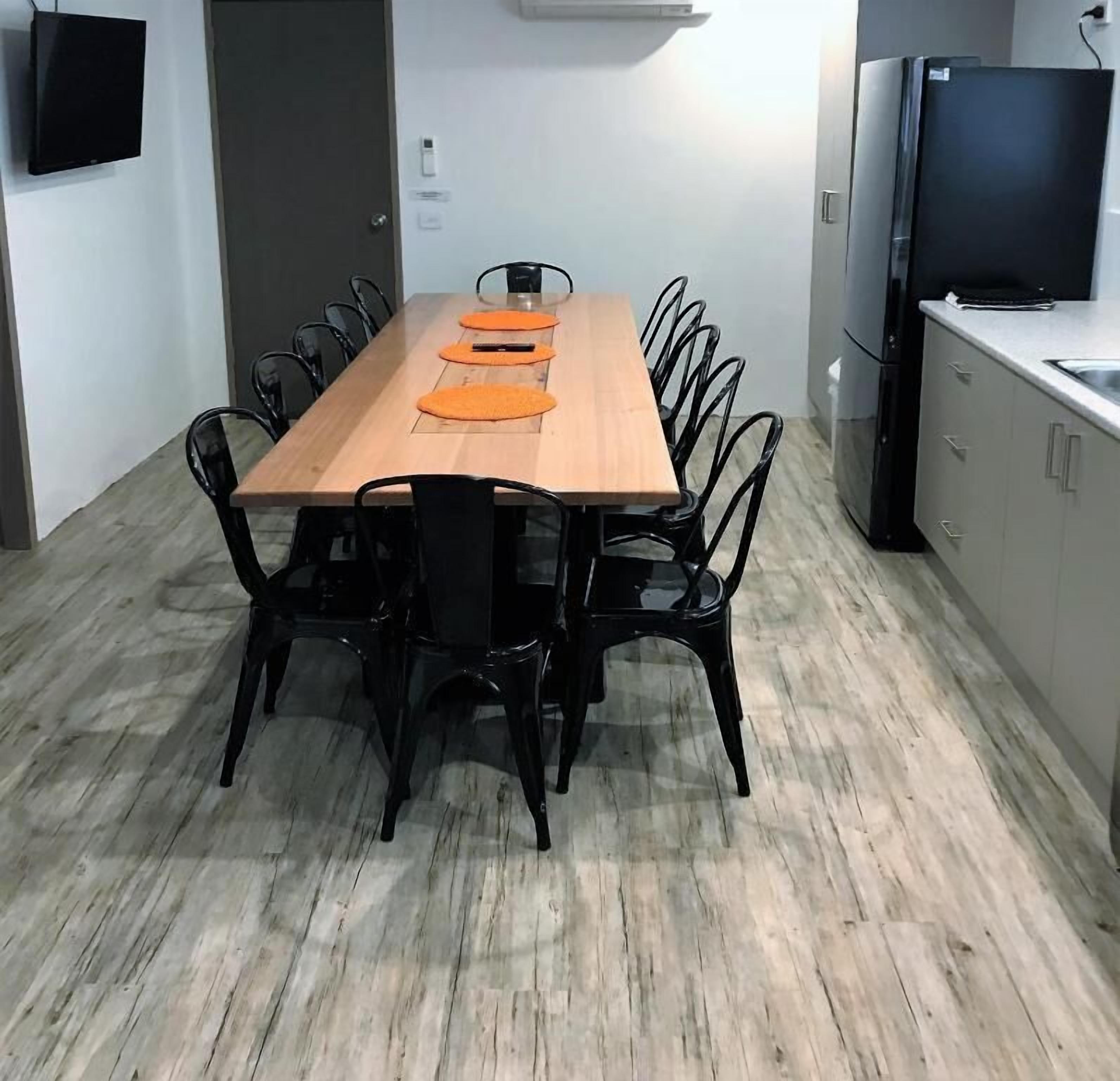 A modern kitchen with a wooden dining table, black chairs, and a built-in TV.