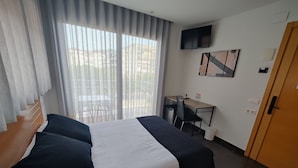 A hotel room with a bed, a desk, a chair, a TV, and a door.