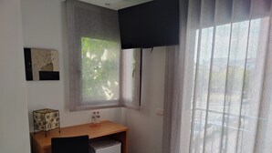 A small, modern room with a desk, chair, and a window with sheer curtains.