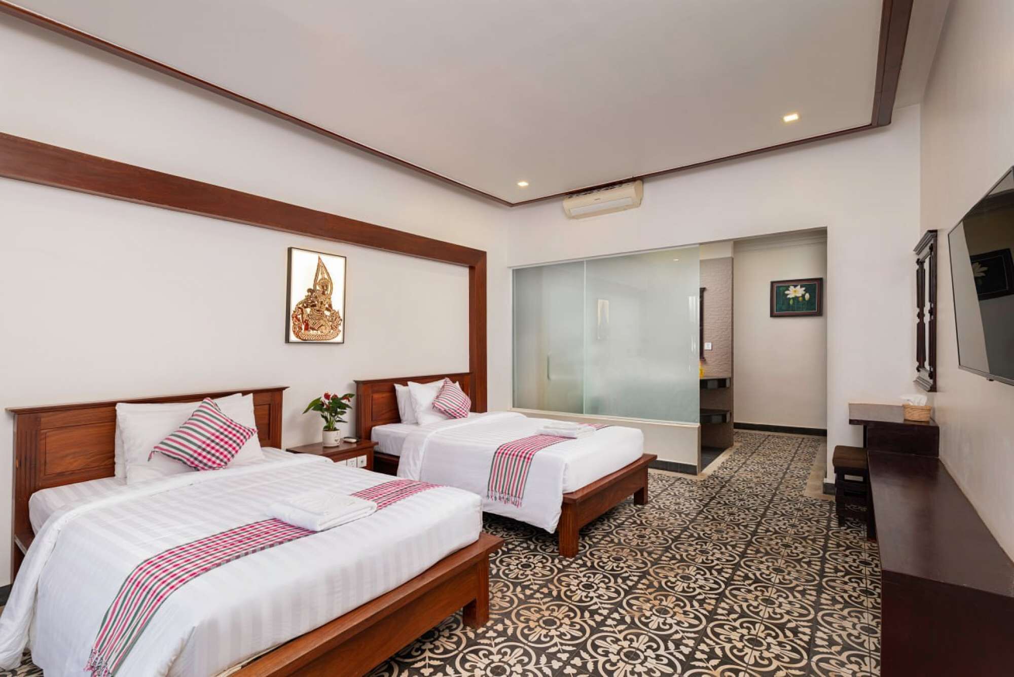 A hotel room with two beds, a large mirror, a television, and a patterned floor.