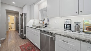 A modern kitchen with white cabinets, stainless steel appliances, a marble countertop, and a dishwasher. - Sea La Vie | Salt Pool & built in Spa in great location (Sarasota)