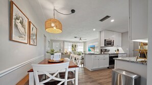A modern kitchen with white cabinetry, a dining area with a wooden table and white chairs, and a central island with a sink. - Sea La Vie | Salt Pool & built in Spa in great location (Sarasota)
