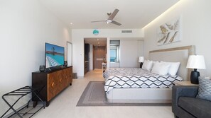 A modern hotel room with a bed, bedside lamps, a TV, a dresser, and a view of the ocean. - One 1402B Hotel Room: New Beachfront Resort, Style & Comfort (Puerto Peñasco)