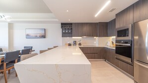 Una cocina moderna con una isla de mármol, armarios de madera y electrodomésticos de acero inoxidable, además de un comedor con sillas.