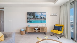 Un moderno salón con vista a la piscina, un sillón amarillo y un cuadro enmarcado con una escena de playa.