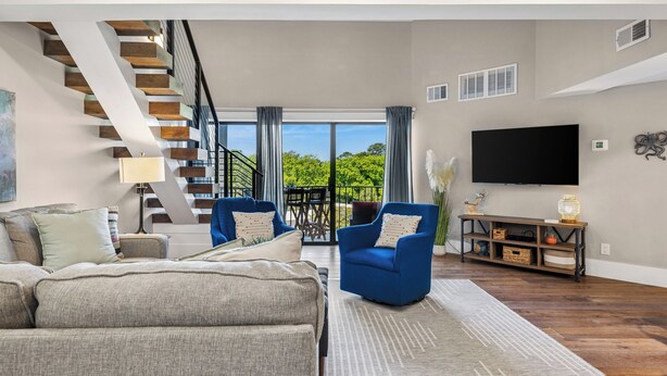 A modern living room with a staircase, a sofa, a blue armchair, a TV, and a console table.