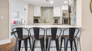 A modern kitchen with a marble backsplash, a central island with bar stools, and a dining area with a sofa and pillows.