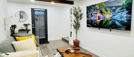 Un salón moderno con un sofá gris, una alfombra colorida y un televisor que muestra una imagen panorámica.