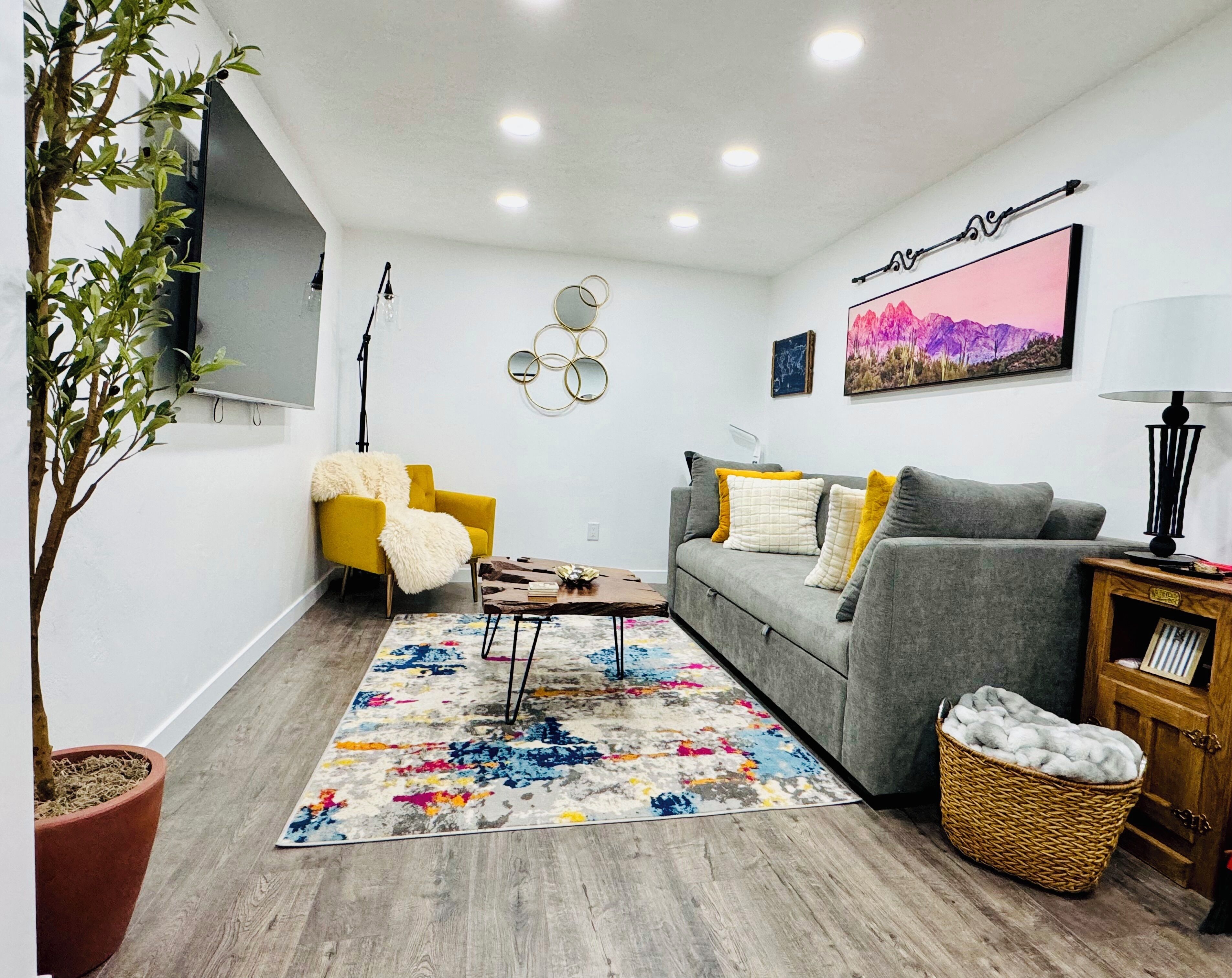 Ein modernes Wohnzimmer mit einem grauen Sofa, einem gelben Sessel und einem farbenfrohen Teppich.