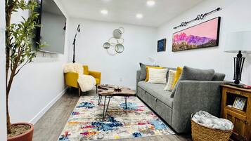 Ein modernes Wohnzimmer mit einem grauen Sofa, einem gelben Sessel und einem farbenfrohen Teppich.
