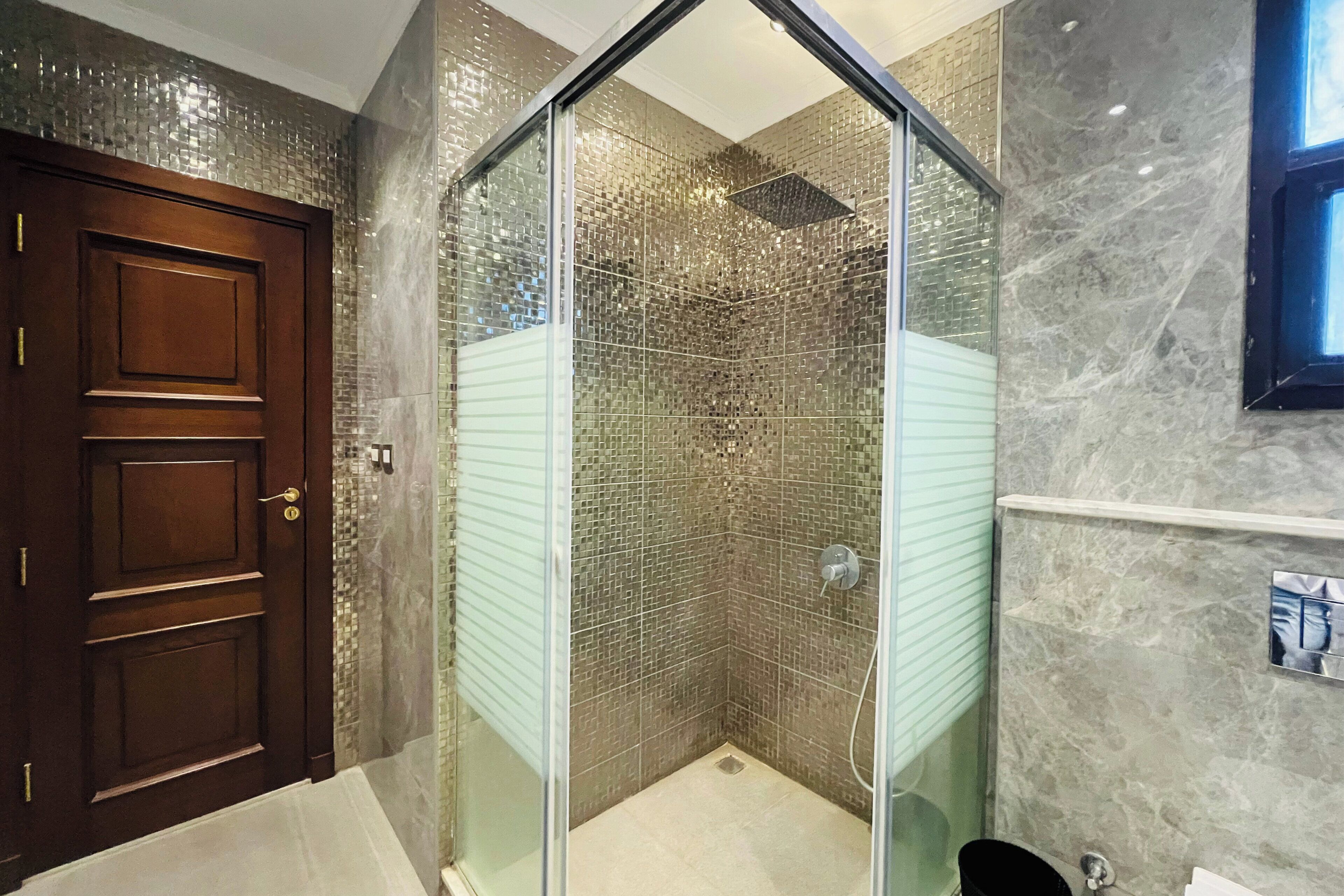 A bathroom with a glass-enclosed shower, a wooden door, and a marble wall.