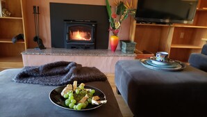 En hyggelig stue med pejs, fjernsyn og spiseområde med en skål druer og ost.