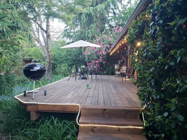 Une terrasse en bois équipée d’un barbecue, de mobilier d’extérieur et de guirlandes lumineuses.