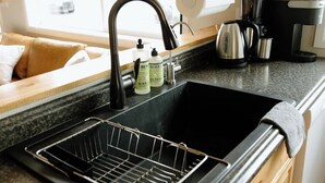 A kitchen with a black sink, wooden cabinets, a stainless steel kettle, and a coffee maker. - Willow South Cottage (Moscow)