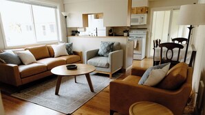 A cozy living room with a sofa, armchair, and coffee table, a kitchen area with appliances, and a dining area with chairs and a table. - Willow South Cottage (Moscow)