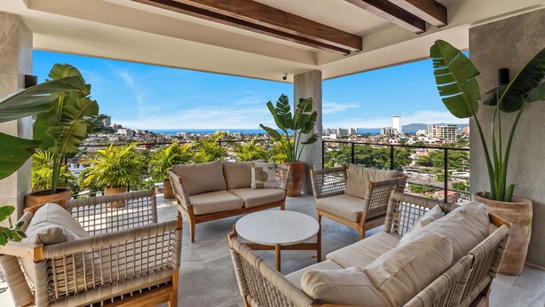 A balcony with wicker furniture, potted plants, and a city view. - Casa Formosa · Modern 2BR + Rooftop Pool (Puerto Vallarta)